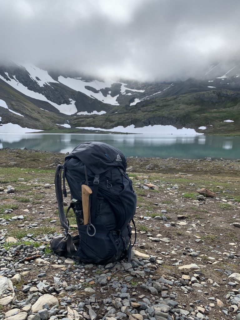 Backpack placed on rocky ground with an alpine lake and snow-capped mountains in the background