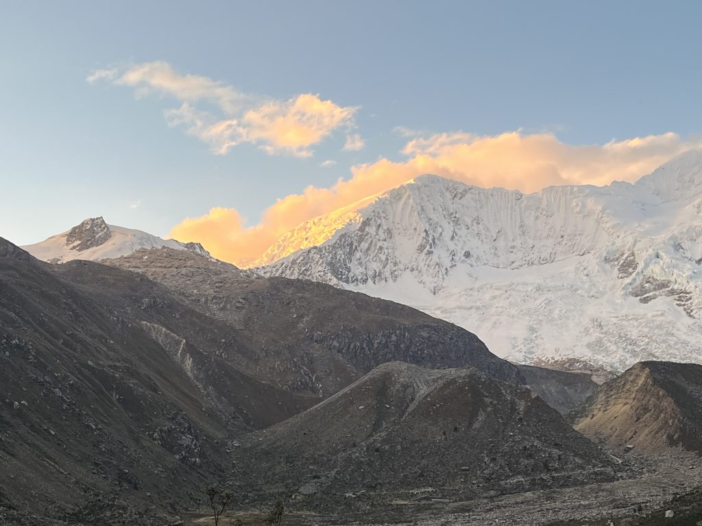 Snowy mountain peaks glowing in the warm light of sunset, with vibrant orange clouds in the sky