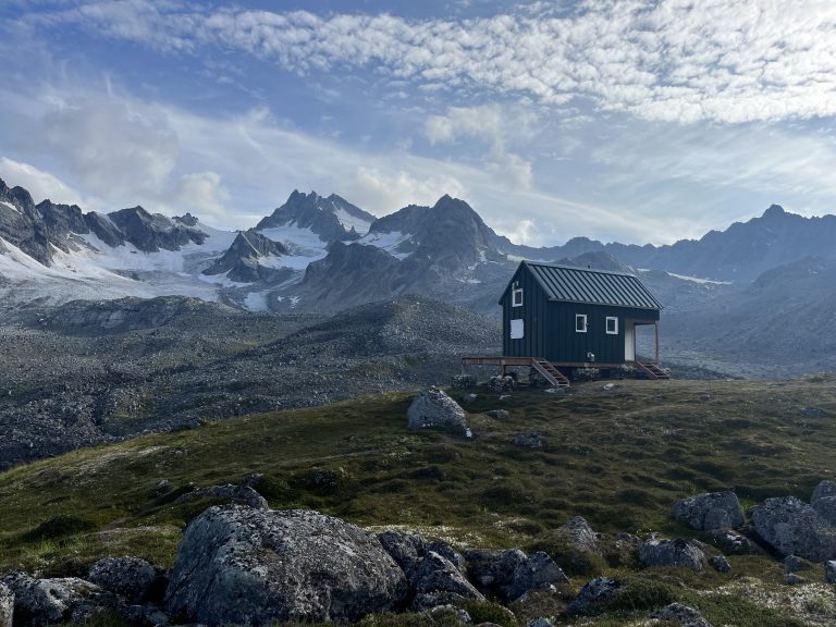 Small green cabin surrounded by a vast mountain landscape and glaciers