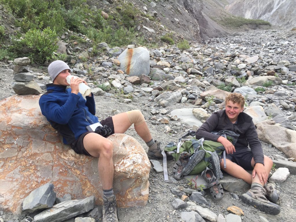 Noam and Avi sit after a long hike on rocks and drink water and laugh