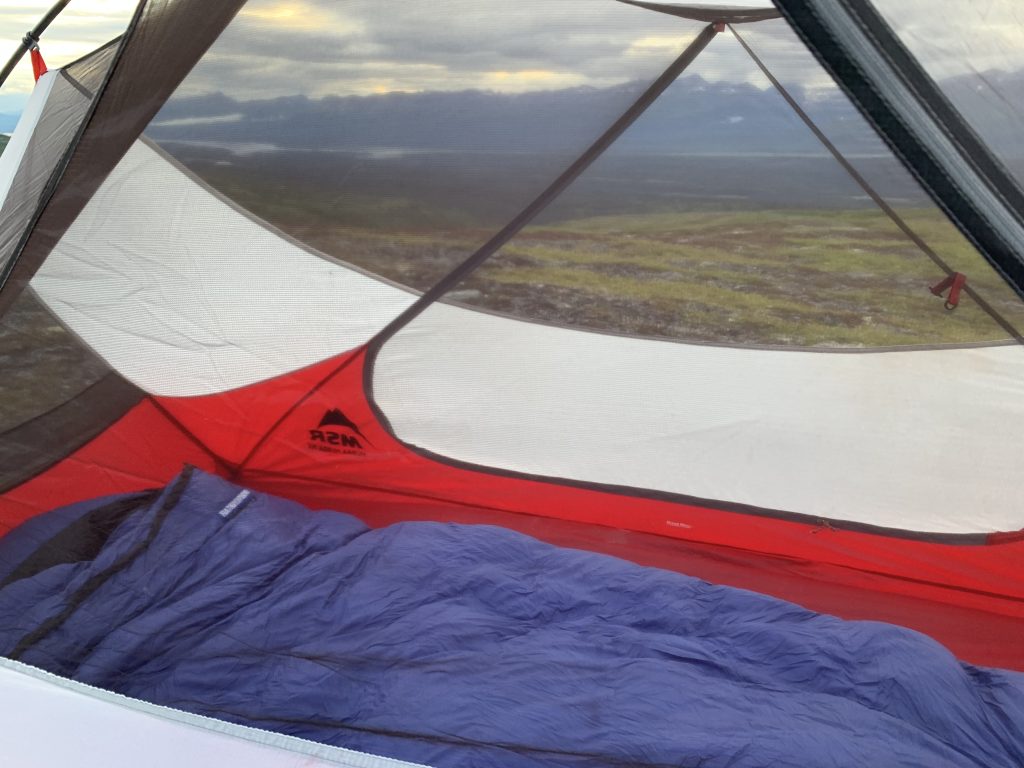 A blue sleeping bag lies inside an MSR tent with an open view of a misty, mountainous landscape in the background