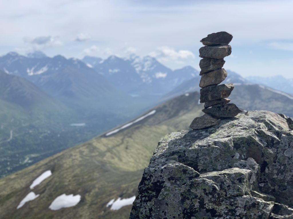 Stone cairn on a mountain summit with a background of snow-capped mountains