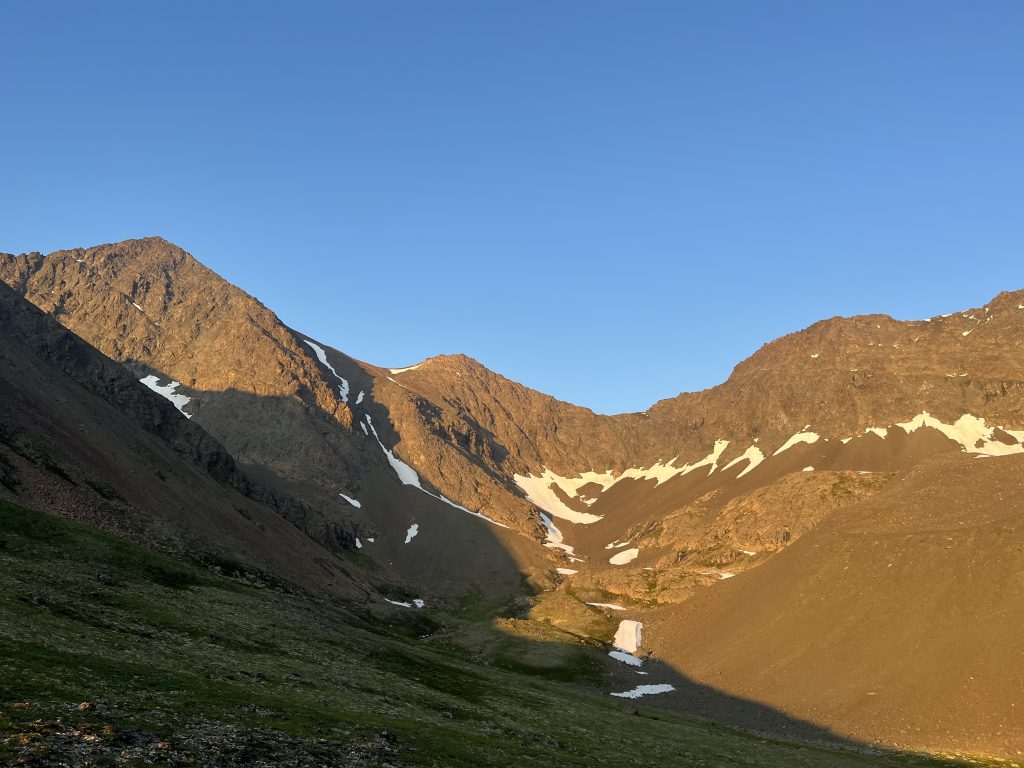 Rocky mountain peaks with patches of snow under a clear evening sky