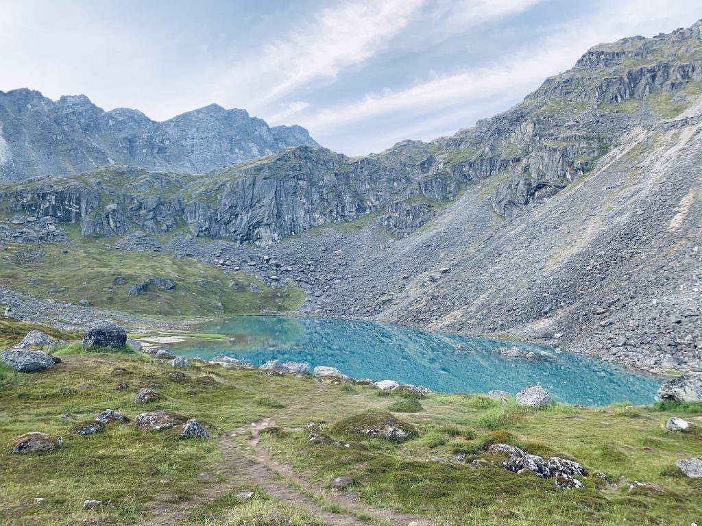 Path leading to Upper Reed Lake with clear blue water, surrounded by steep rocky walls and green landscape.