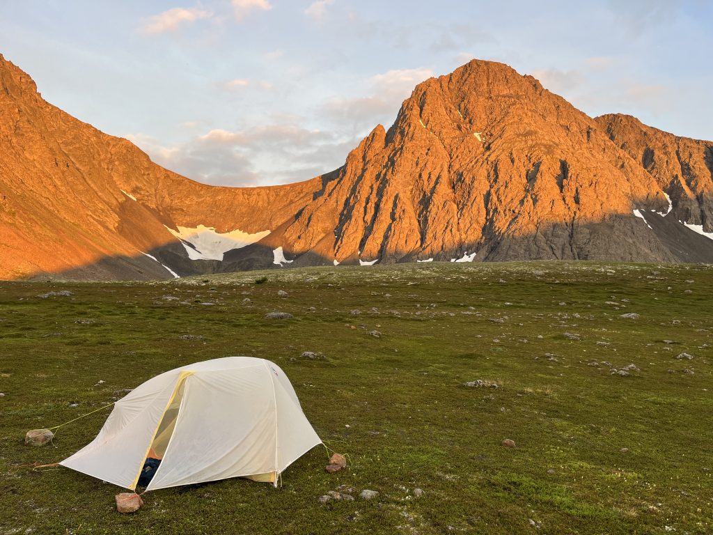 Tent set up on green grass with South Suicide Peak in the background, illuminated by a golden sunset.