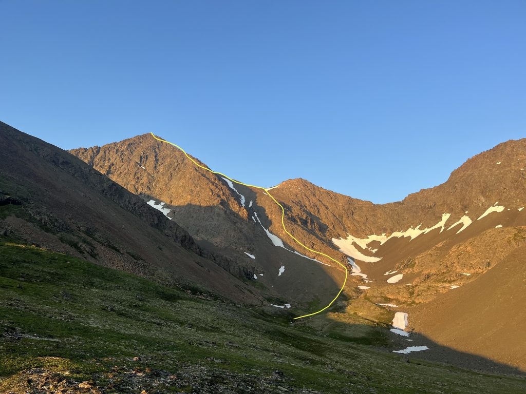 Rocky mountain peaks with patches of snow under a clear evening sky, with climbing route