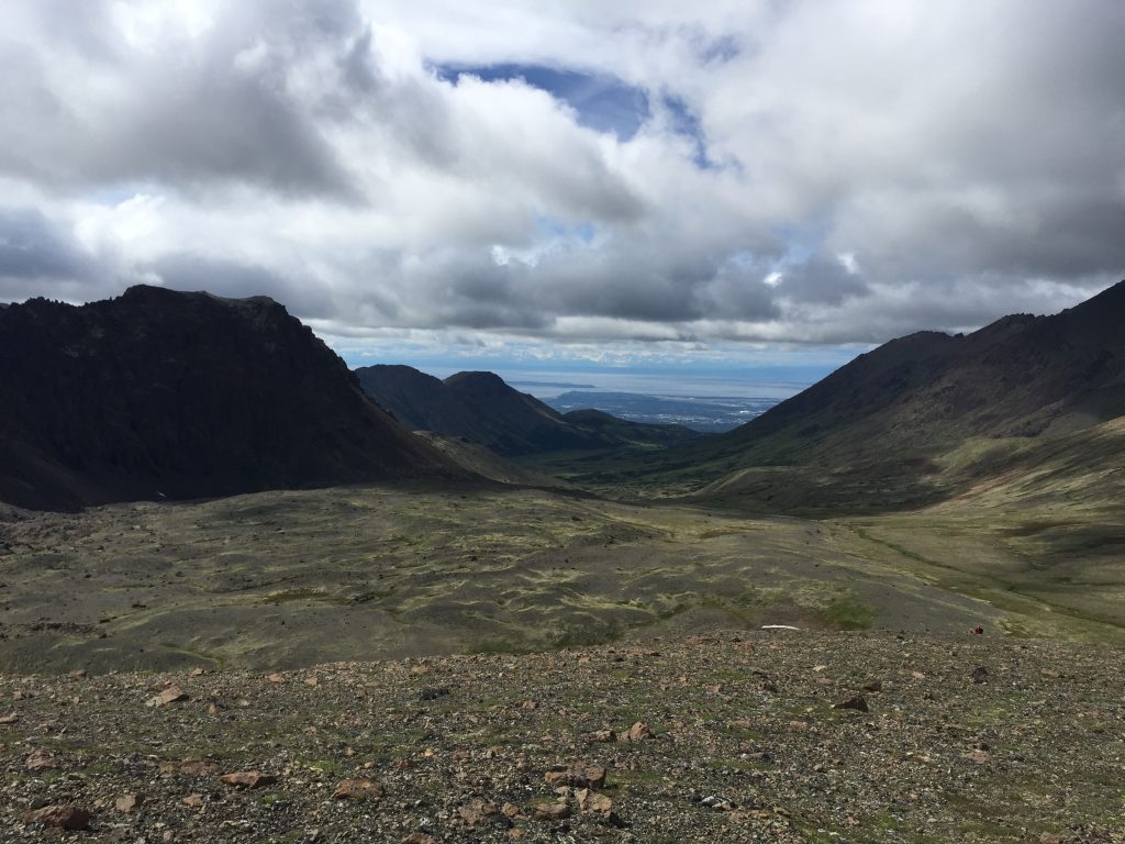 View from Hidden Lake in Anchorage, Alaska, looking down a wide valley with mountains in the distance and a cloudy sky overhead.