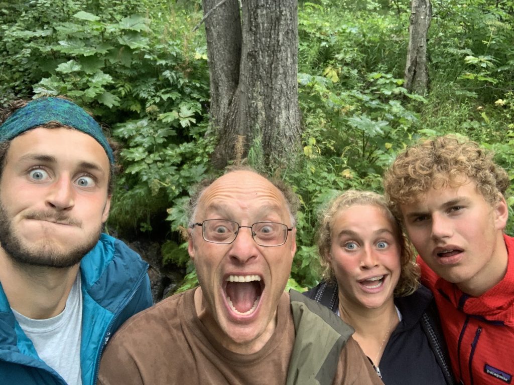 Family selfie after a hike with four people making funny faces – Noam, Avi, Leah, and Aryeh – surrounded by lush green foliage