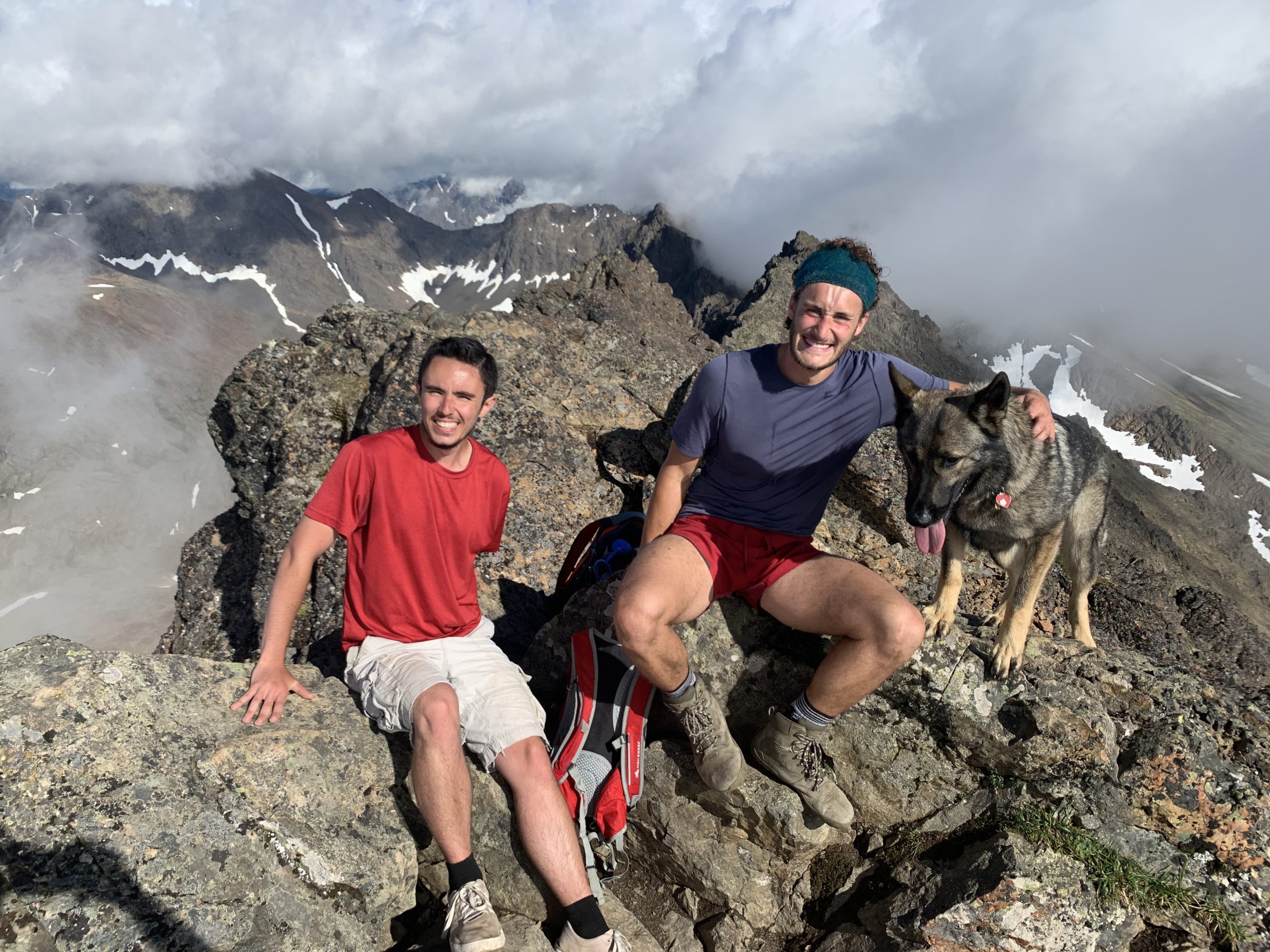 Noam and Kyle and my dog, Akko sitting on the summit of Big O'Malley Peak with cloud-covered mountains behind