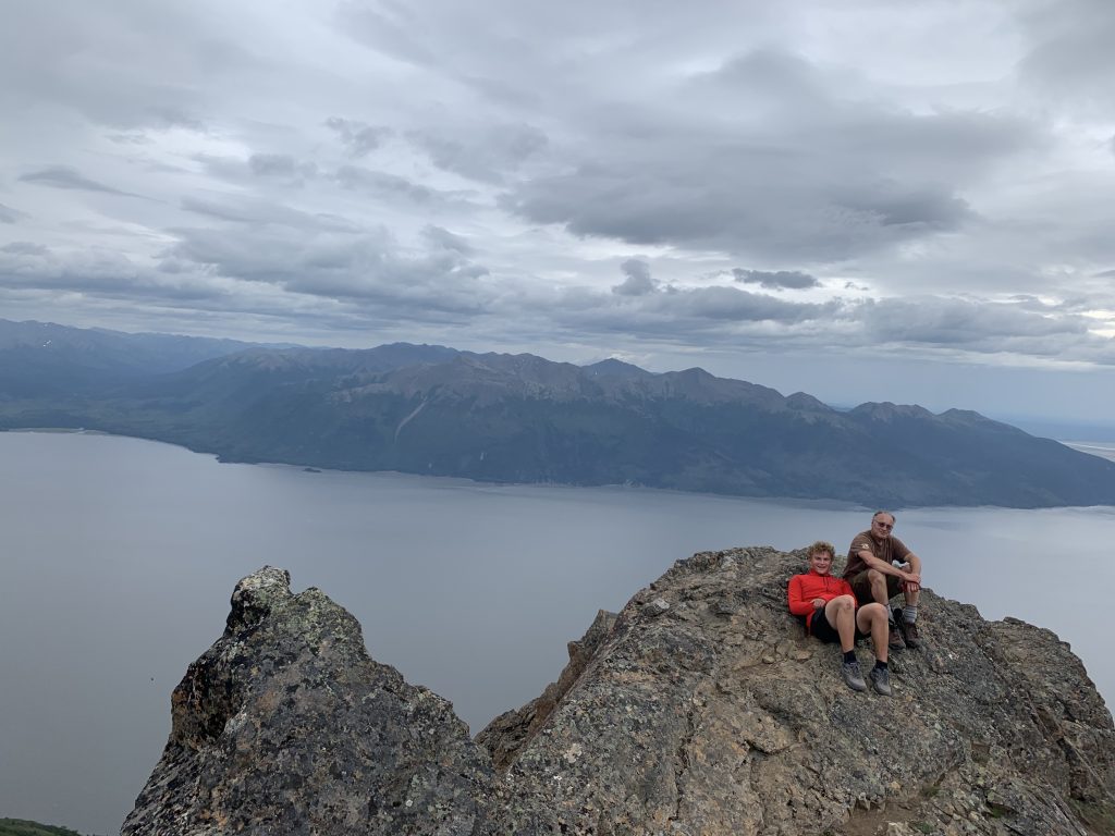 My dad and Avi rest on the rocky summit of McHugh Peak in Anchorage, Alaska, with an ocean and mountain backdrop