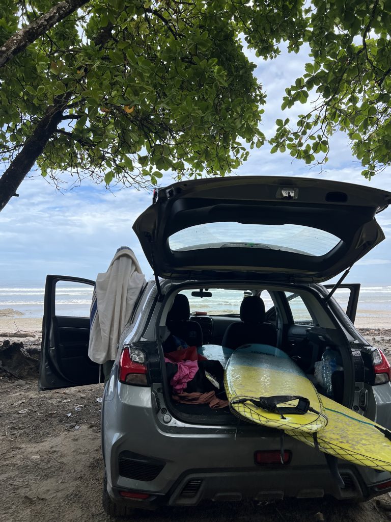 Car parked by a beach in Costa Rica with a surfboard in the trunk, ready for a day of surfing