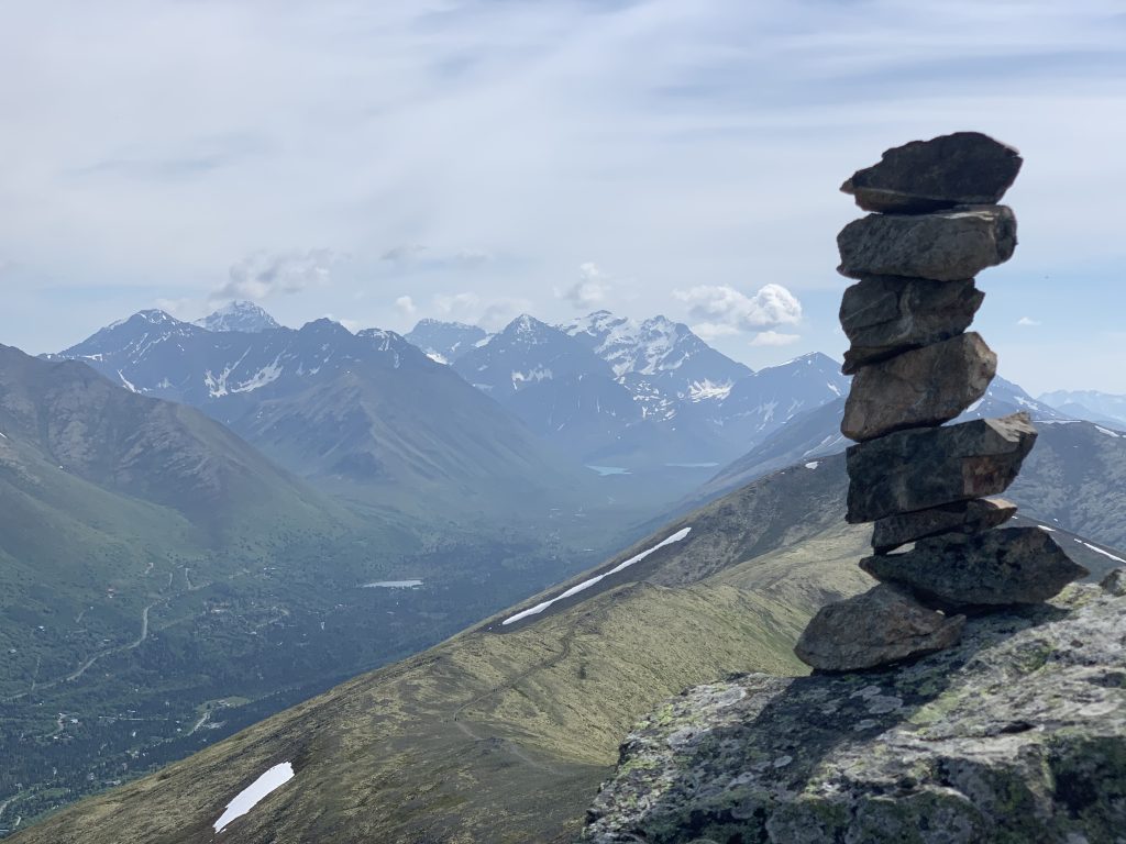 Stacked rocks on Rendezvous Peak with a view of Eagle River Valley and surrounding mountains in Alaska