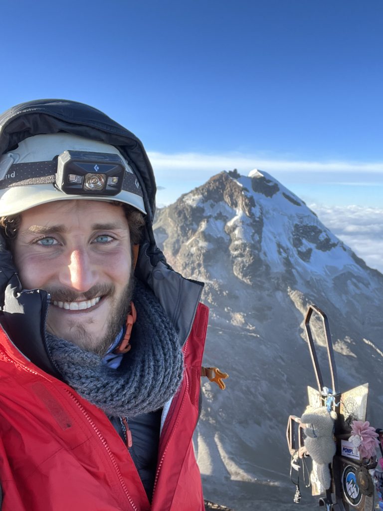 Climber smiling on the summit of Illinizas North with Illinizas South in the background