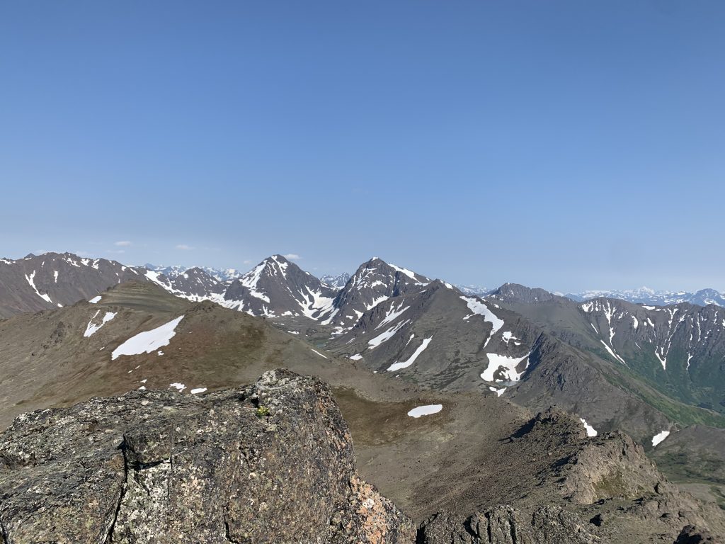 View of snow-dusted mountains and valleys from the summit of McHugh Peak in Anchorage, Alaska, under a clear blue sky