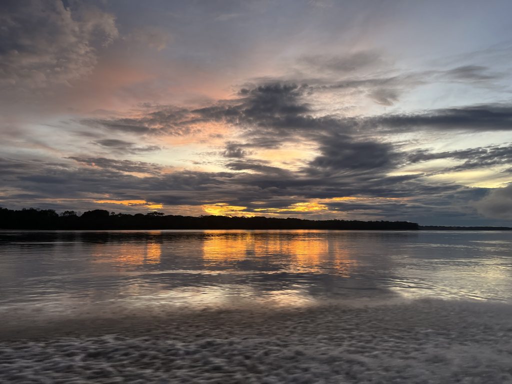 Sunset over the Napo River, with clouds reflecting warm hues on the water’s surface