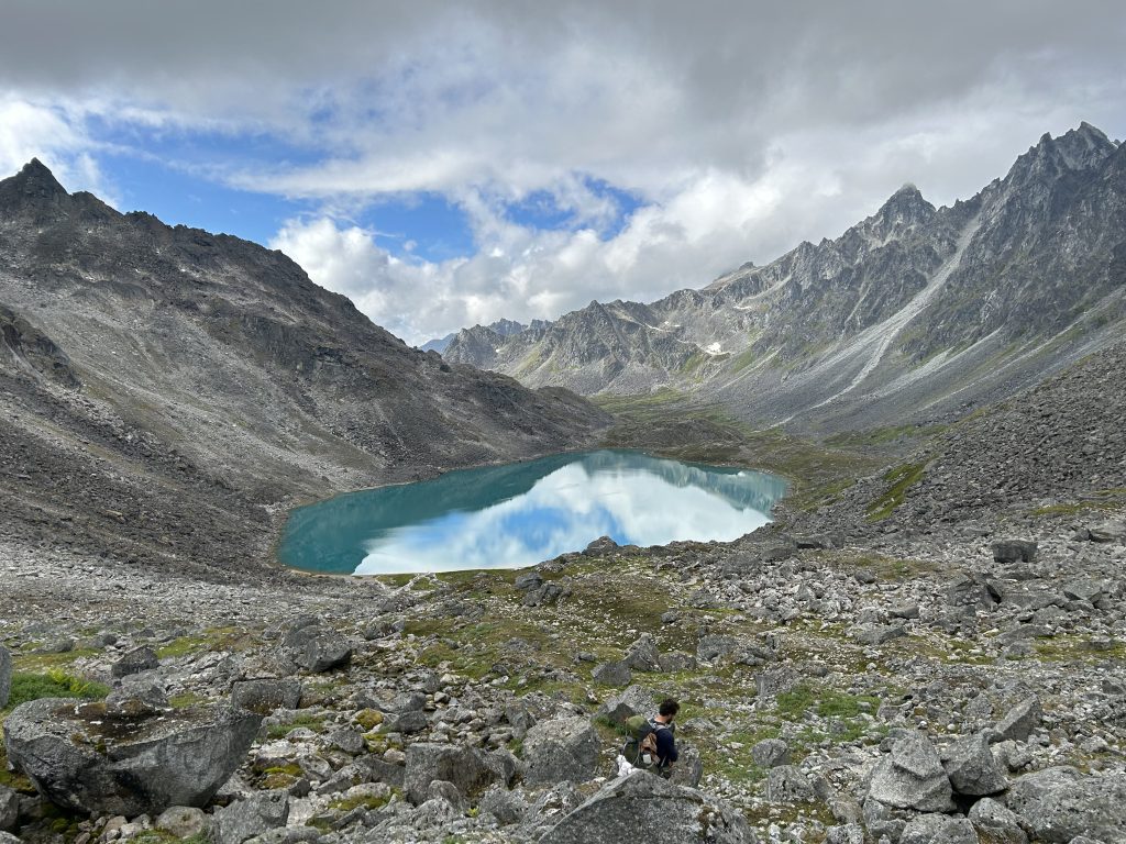 Turquoise Upper Reed Lake surrounded by rocky mountains and steep slopes under a partly cloudy sky.