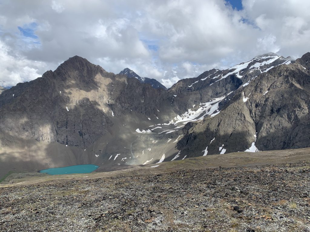 Panoramic view of Triangle Peak and surrounding mountains, with a turquoise glacial lake nestled in the valley below and snow patches on the peaks