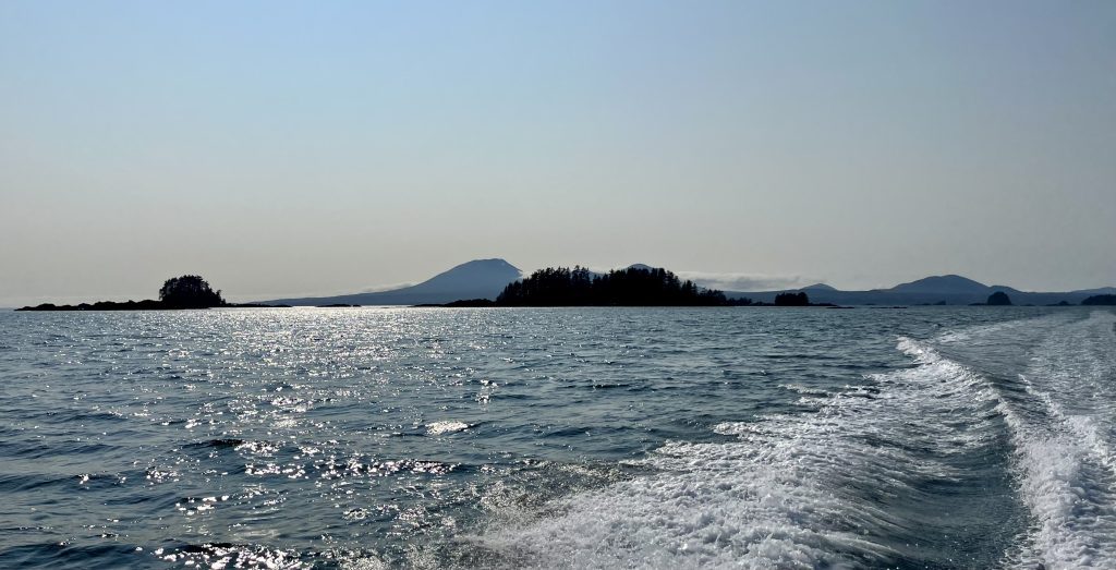 Sitka Sound’s calm waters with distant islands and Mount Edgecumbe under a blue sky. Caption: Sitka Sound sparkles under a rare sunny day, with Mount Edgecumbe and forested islands in the distance.