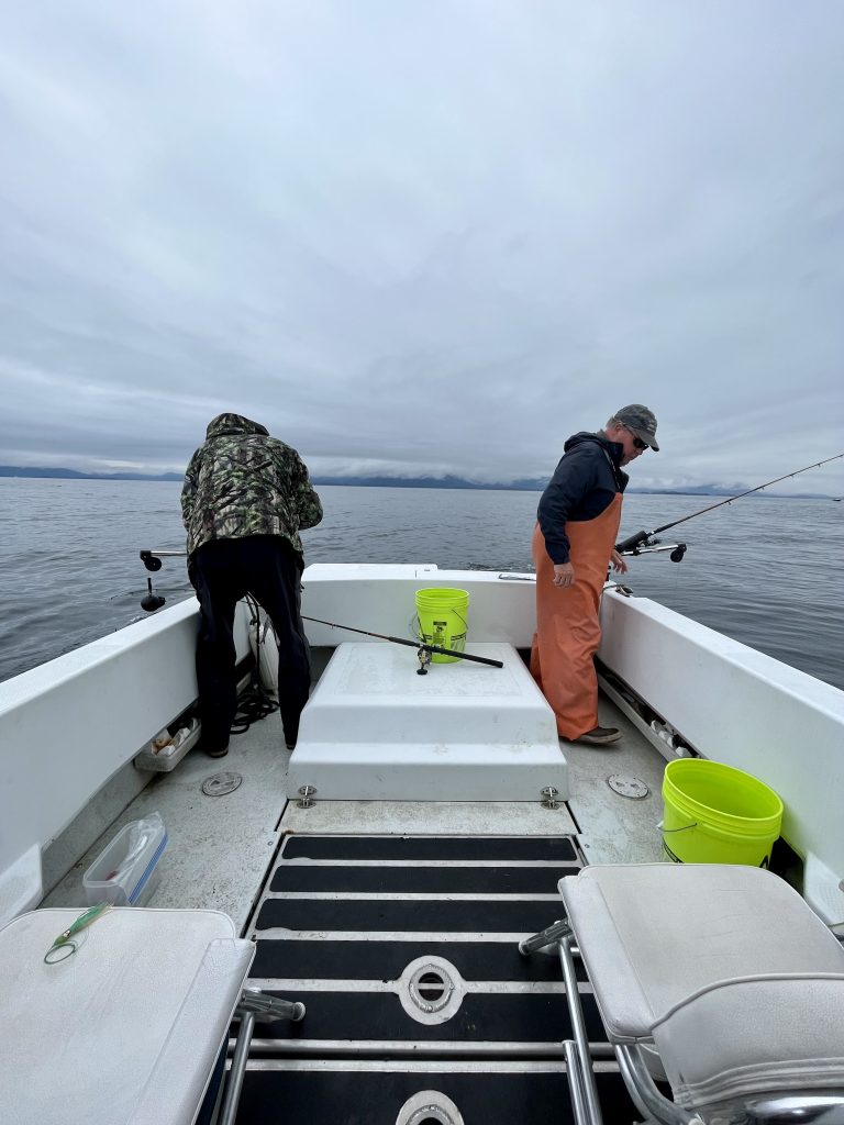 Two people on a boat fishing in calm waters under a cloudy sky in Sitka, Alaska.