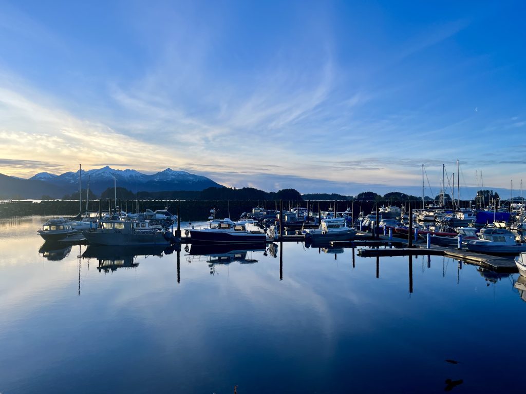 Boats docked in Sitka’s harbor reflecting off calm waters with mountains in the background.