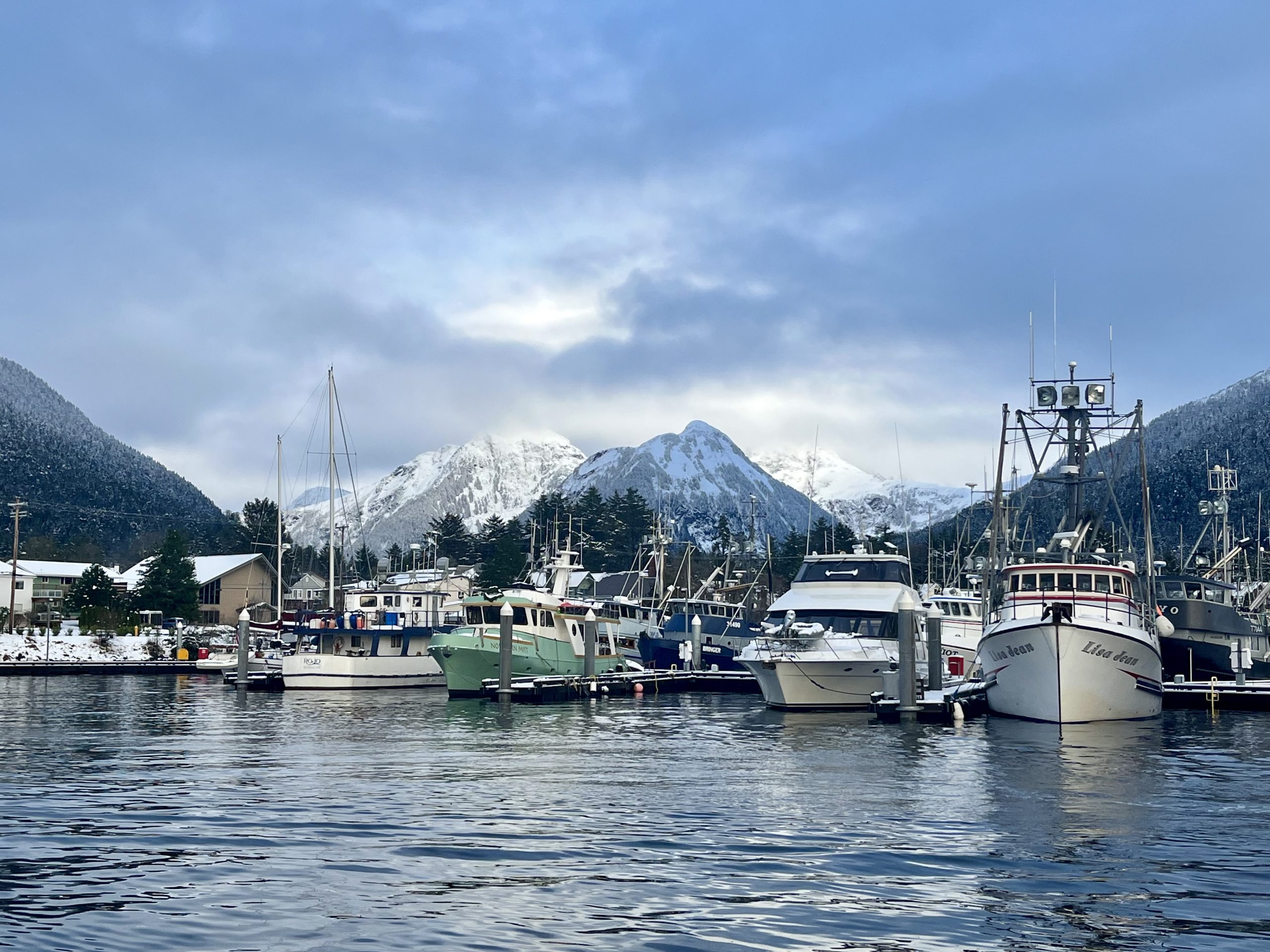 A view of Sitka’s harbor with fishing boats docked and snow-covered mountains in the background.